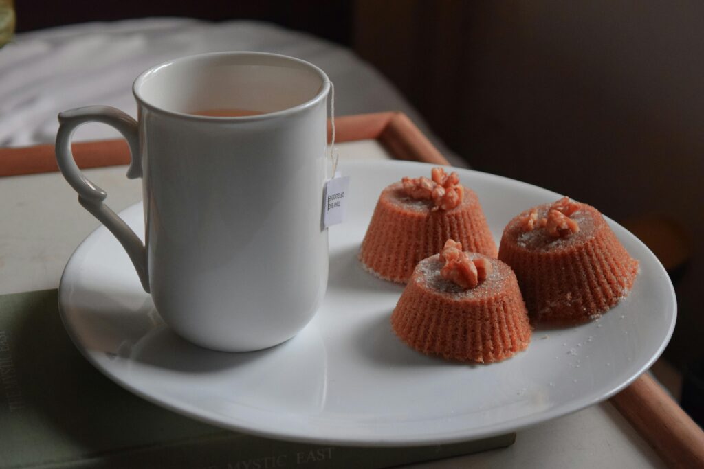 Sweet yummy chocolate cupcakes topped with walnuts and placed on white plate with fresh hot tea served on tray
