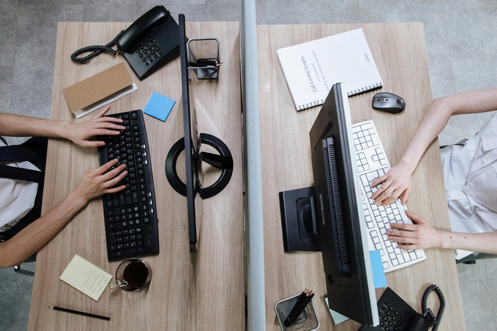 Top view of two workstations with people typing on keyboards, during the day in an office setting.